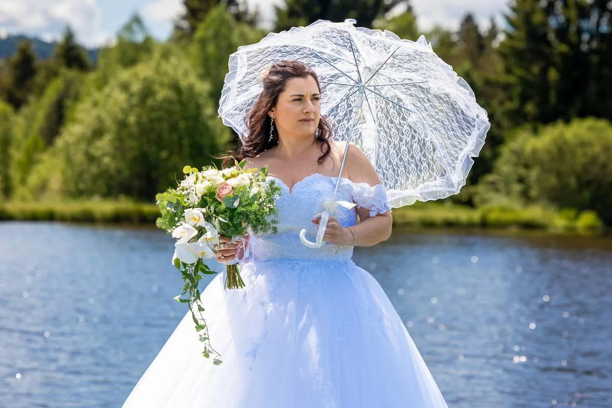 Mariée tenant une ombrelle en dentelle au bord de l'eau